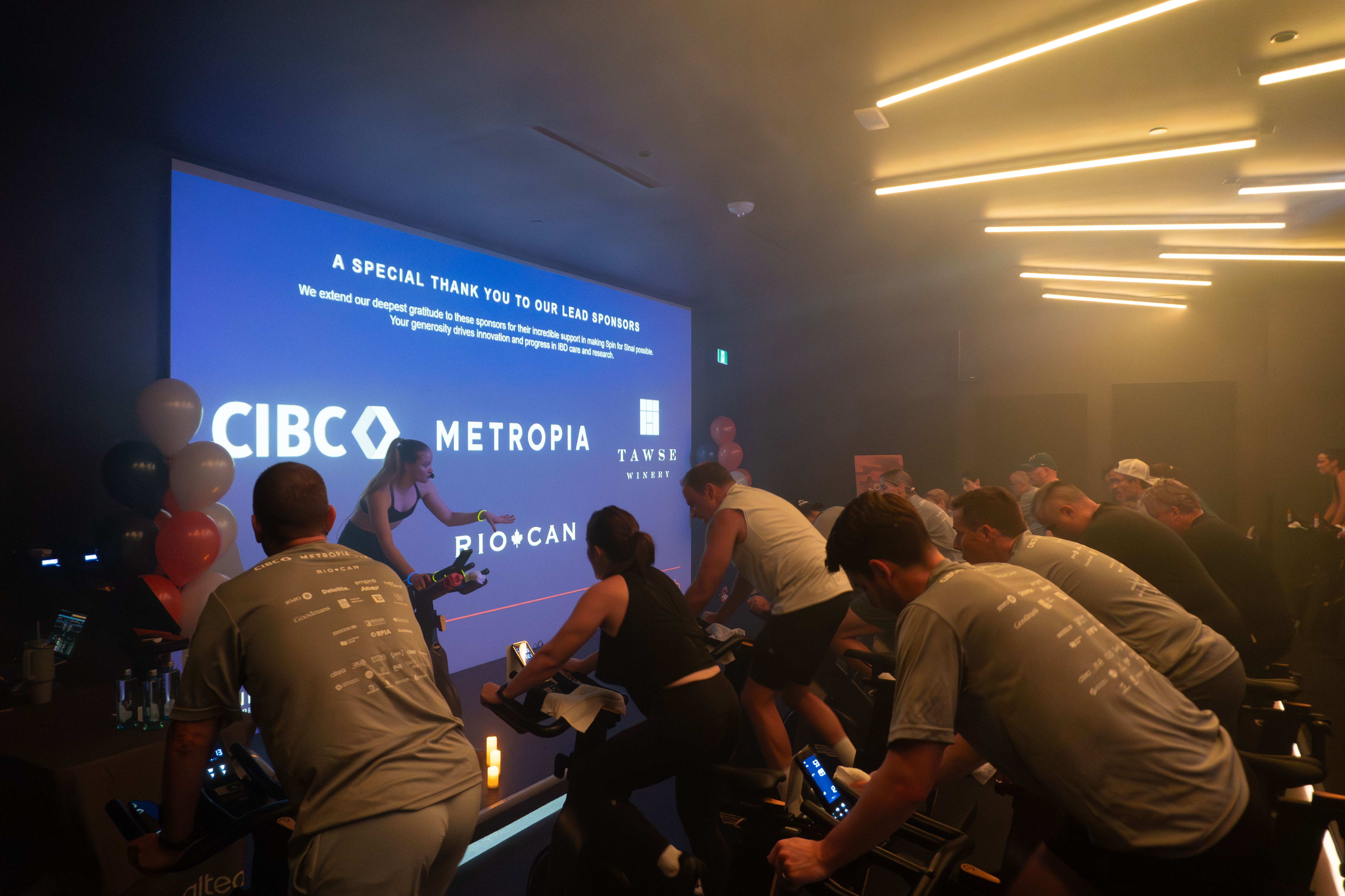 Spin class with riders facing a screen with corporate logos
