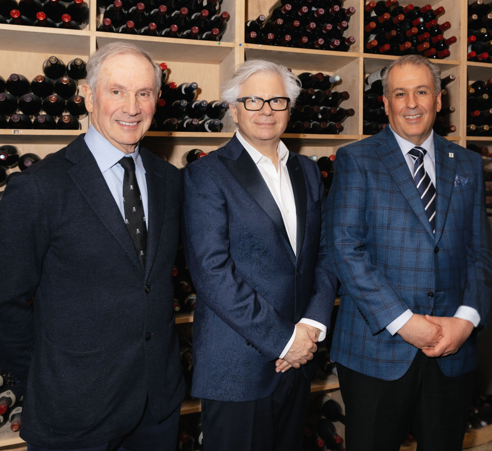 three men standing in front of a wine collection