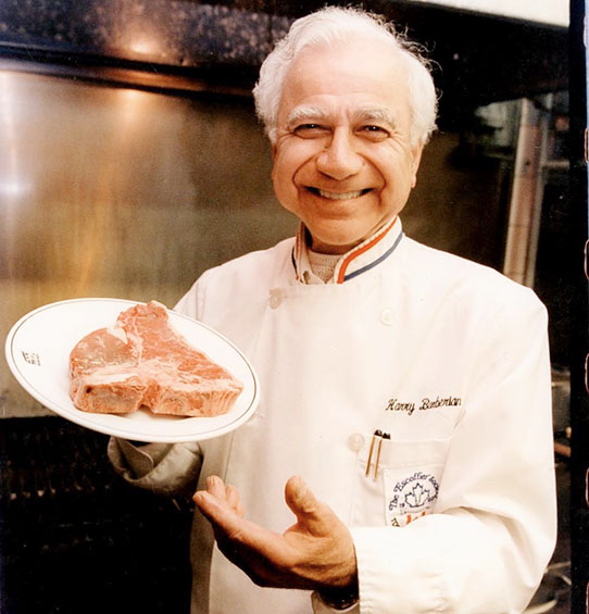 Older man in chef uniform holding a large steak